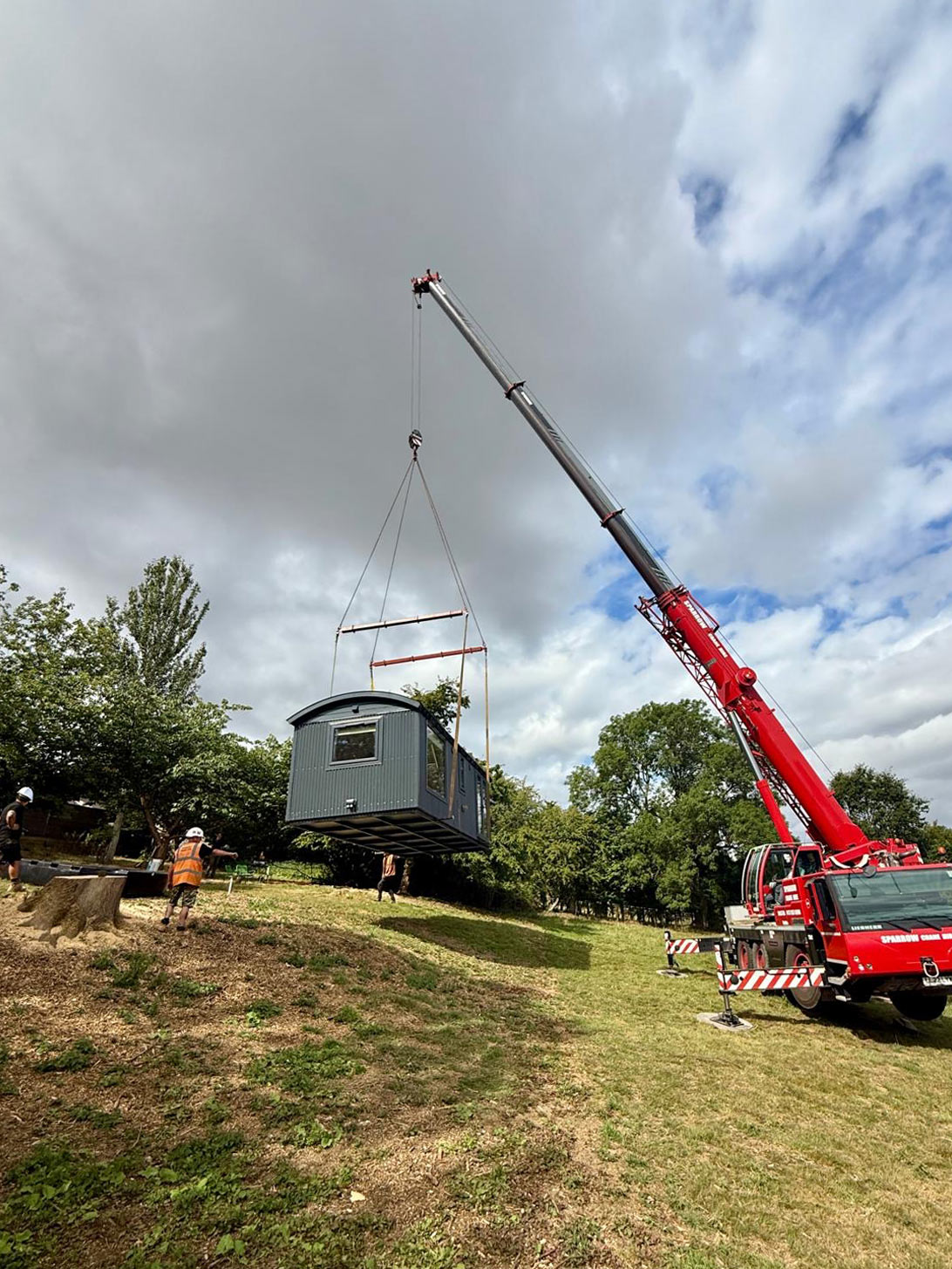 Crane lifting a luxury shepherd hut into position at a countryside location with precision rigging